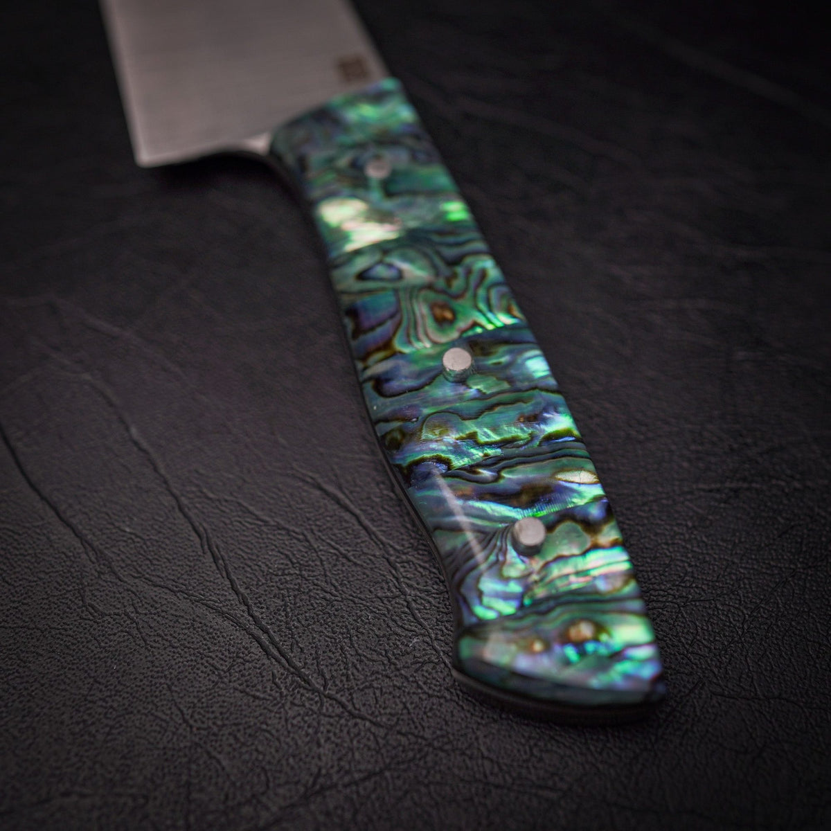 Macro of a shimmering green-blue abalone handle on black leather