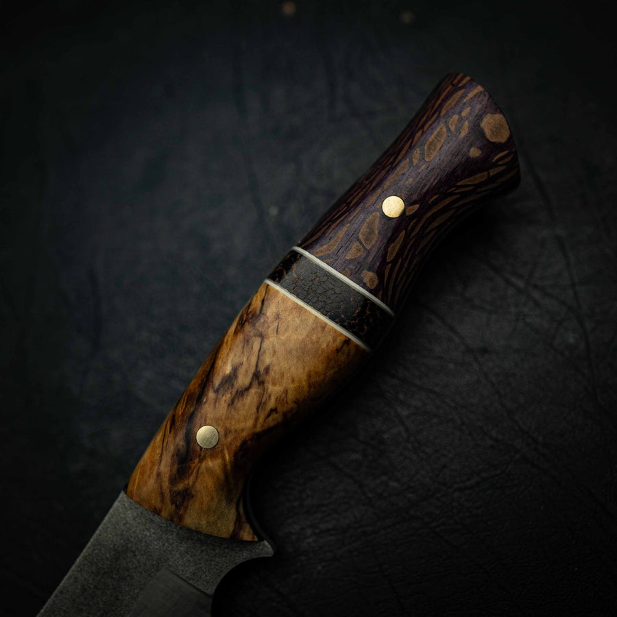 Close-up of a handle made from swirling burl and dark timber with brass pins