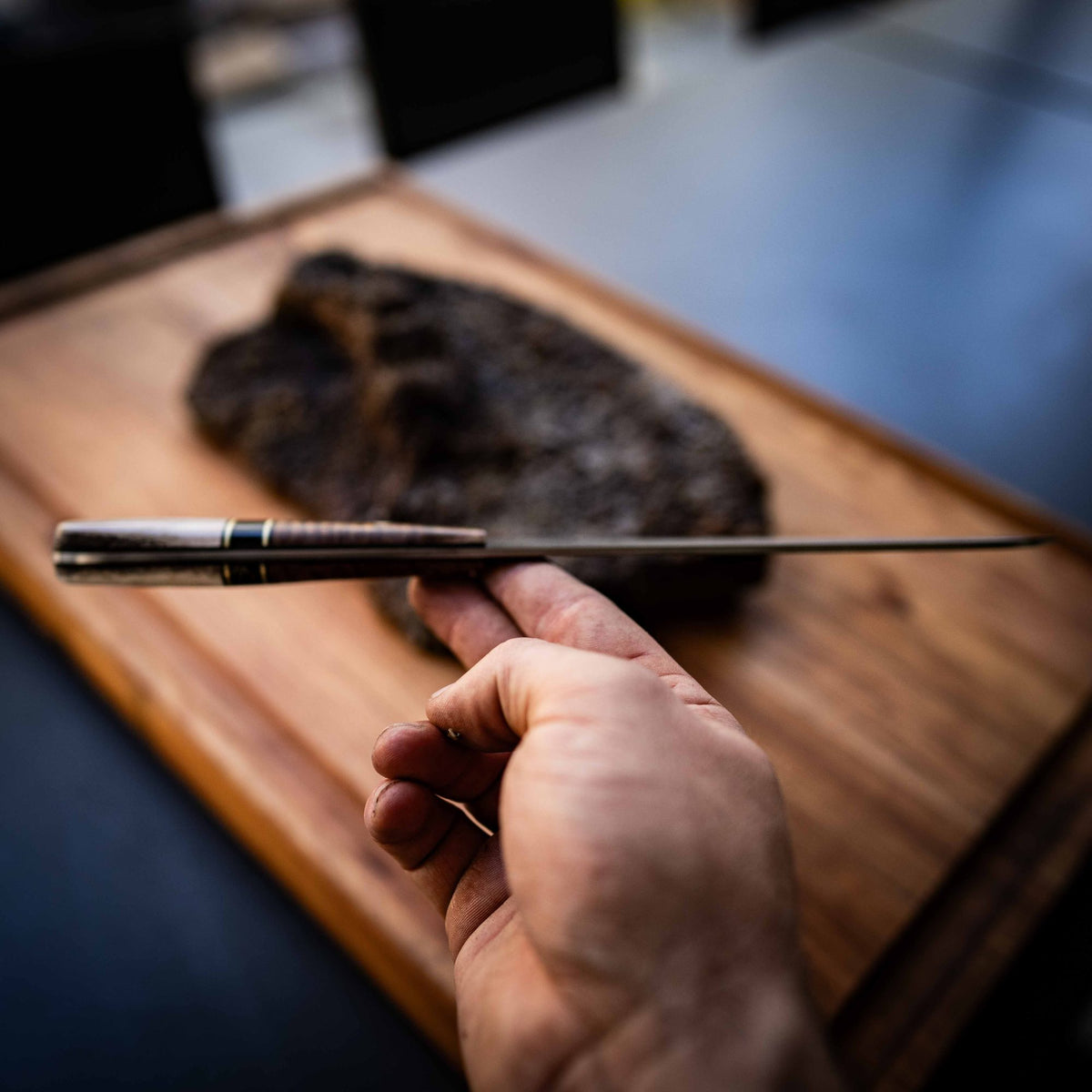A hand holds a long slicer beside a smoked brisket on a timber board