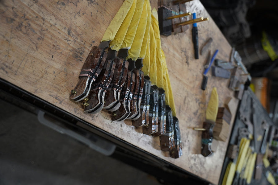 A batch of unfinished blades wrapped in tape, lined up on a workshop bench among tools