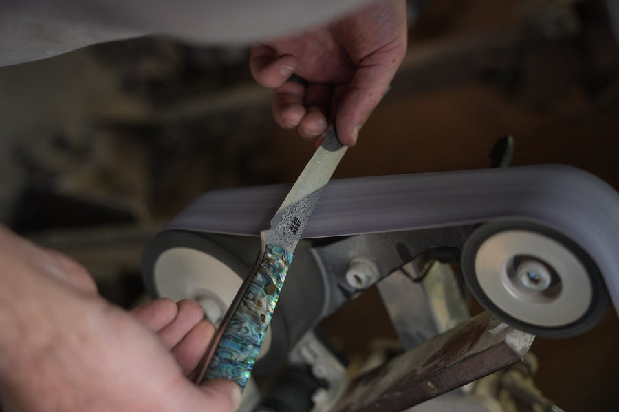 Hands shaping a shimmering abalone handle on a grinding wheel