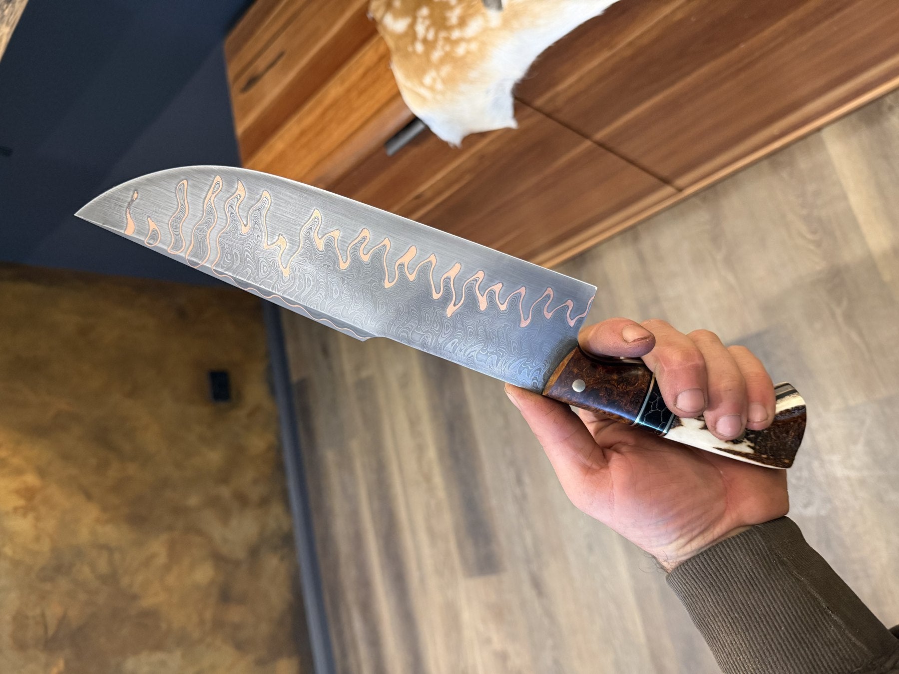 A one-off Iron Gate Knives custom knife with a copper clad Damascus blade and burl handle, held in hand